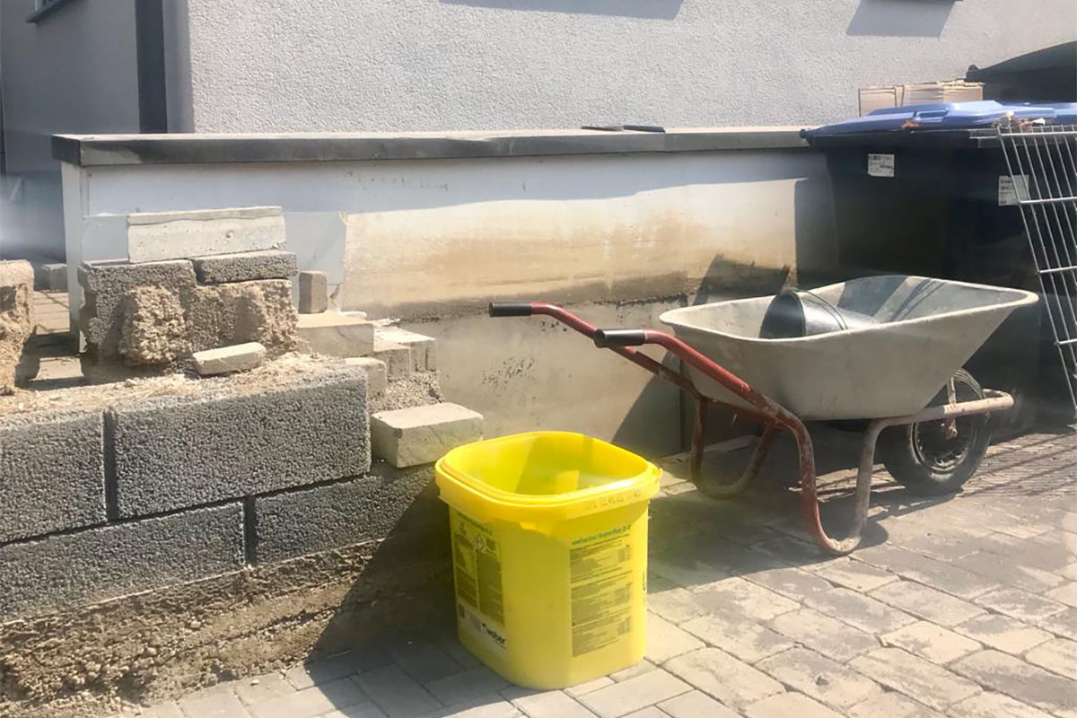 Ein gelber Eimer und eine Schubkarre vor einer Baustelle